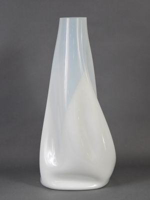 un vase en verre blanc au fond incurvé, posé sur une surface grise