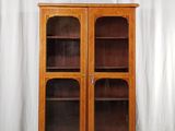 une vieille armoire en bois avec des portes vitrées et un rideau blanc derrière