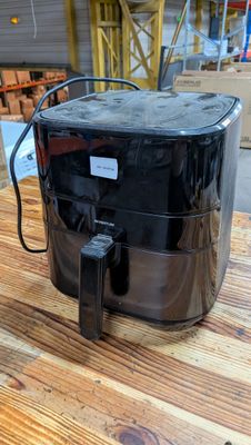 une friteuse à air chaud noire posée sur une table en bois dans un entrepôt