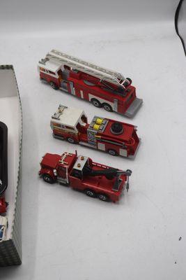 Plusieurs camions de pompiers miniatures sont rangés dans une boîte posée sur une table