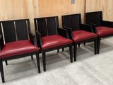 quatre chaises alignées, avec des sièges en cuir rouge, devant un mur en bois
