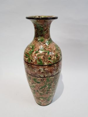 un vase vert et marron posé sur une surface blanche