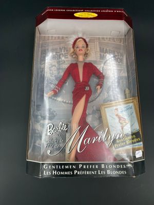 La poupée se trouve dans une boîte sur laquelle est représentée une femme en robe rouge.