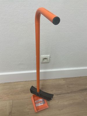 une lampe orange posée sur un parquet, près d'un mur blanc