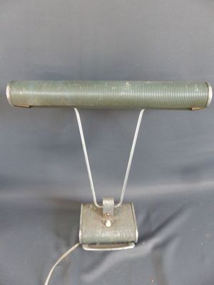 une image représentant une lampe verte posée sur un pied métallique, sur fond gris