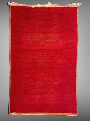 a red rug with fringes hanging on a gray wall