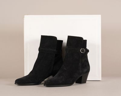 une paire de bottines noires en daim avec des boucles et une boîte blanche