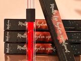 three lip glosses and a box of lipstick on a table