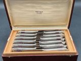 six silver plated knives in a case on a table