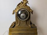 a gold clock on a clear shelf on a white wall