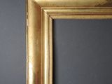 an antique gold frame against a gray wall with a black background