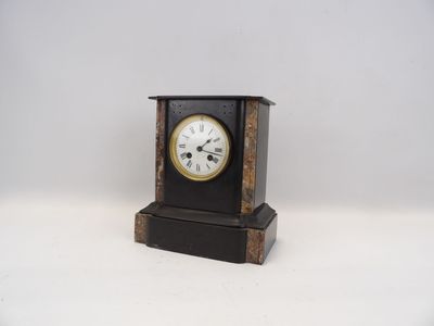 une petite horloge noire avec un cadran blanc sur fond blanc