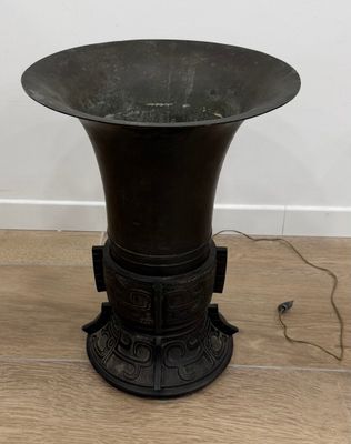 un vase noir posé sur un parquet, près d'un mur blanc