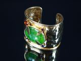 bague en argent ornée d'une feuille verte et de pierres rouges sur un fond noir