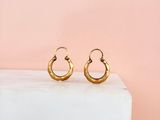 une paire de boucles d'oreilles créoles en or posée sur un bloc de marbre