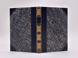 un vieux livre à la couverture noire et aux bordures dorées posé sur une surface blanche