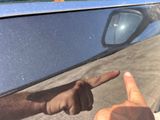 a man pointing at something in the mirror of a car