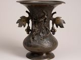 un vase en métal orné d'un oiseau, posé sur une surface blanche