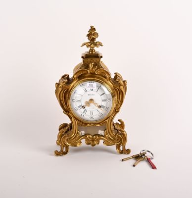 une petite horloge en or posée sur une table, avec un trousseau de clés à côté