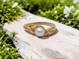 un gros plan d'une bague en or sertie d'une perle, posée sur une surface recouverte de mousse