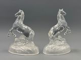 une paire de figurines de chevaux en verre posées sur un rocher, sur fond gris