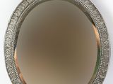 silver plated mirror with ornate design on stand against a white background