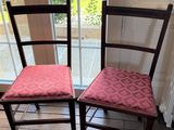 Deux chaises en bois, avec des coussins rembourrés roses, sont placées devant une fenêtre.