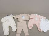 Plusieurs vêtements pour bébé sont disposés sur un lit, avec leurs étiquettes encore attachées.