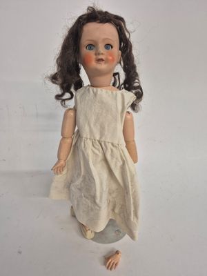 an old doll with a white dress and brown hair on a white surface