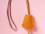 an orange handbag with two metal handles on a pink background