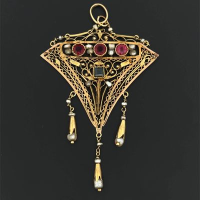 a close up of a gold pendant with red stones and pearls