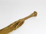 gold feather shaped object on a white surface with a white background