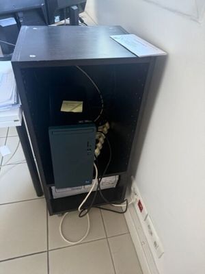 un petit ordinateur noir posé par terre près d'un mur