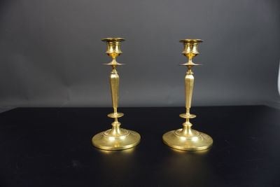 une paire de bougeoirs en laiton posés sur une table noire, sur fond gris