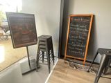 des tables et des tabourets devant un tableau noir sur lequel est inscrit le menu