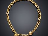 a gold bracelet with two small bells on a black background