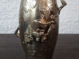 un vase en argent posé sur une table en bois, avec un mur blanc en arrière-plan