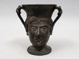 un vase noir orné d'un visage, posé sur une table