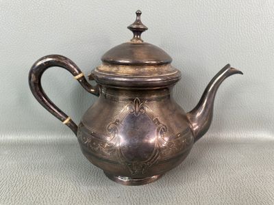 une théière en argent avec son couvercle, posée sur une table