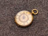 une petite montre de poche en or posée sur un tissu marron