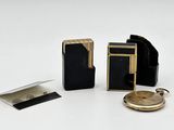 une petite montre de poche noire et dorée, posée à côté d'un portefeuille et d'une autre montre de poche