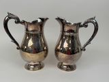 pair of silver plated pitchers with handles on a white surface