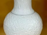 un vase blanc posé sur une table, avec un mur jaune en arrière-plan