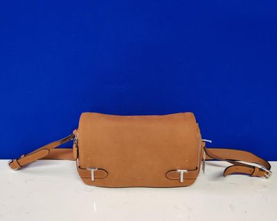 a tan leather cross body bag on a white table