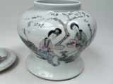 a white vase with a painting on it next to a plate