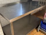 une table en acier inoxydable dans une cuisine, avec une poubelle posée par terre
