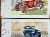 two paintings of old cars on display on a table