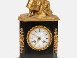 une horloge noire et dorée surmontée d'une statue