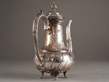 a silver coffee pot sitting on a stand on a table