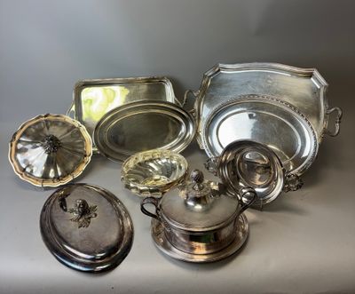 Plusieurs plats et plateaux en métal argenté sont posés sur une table